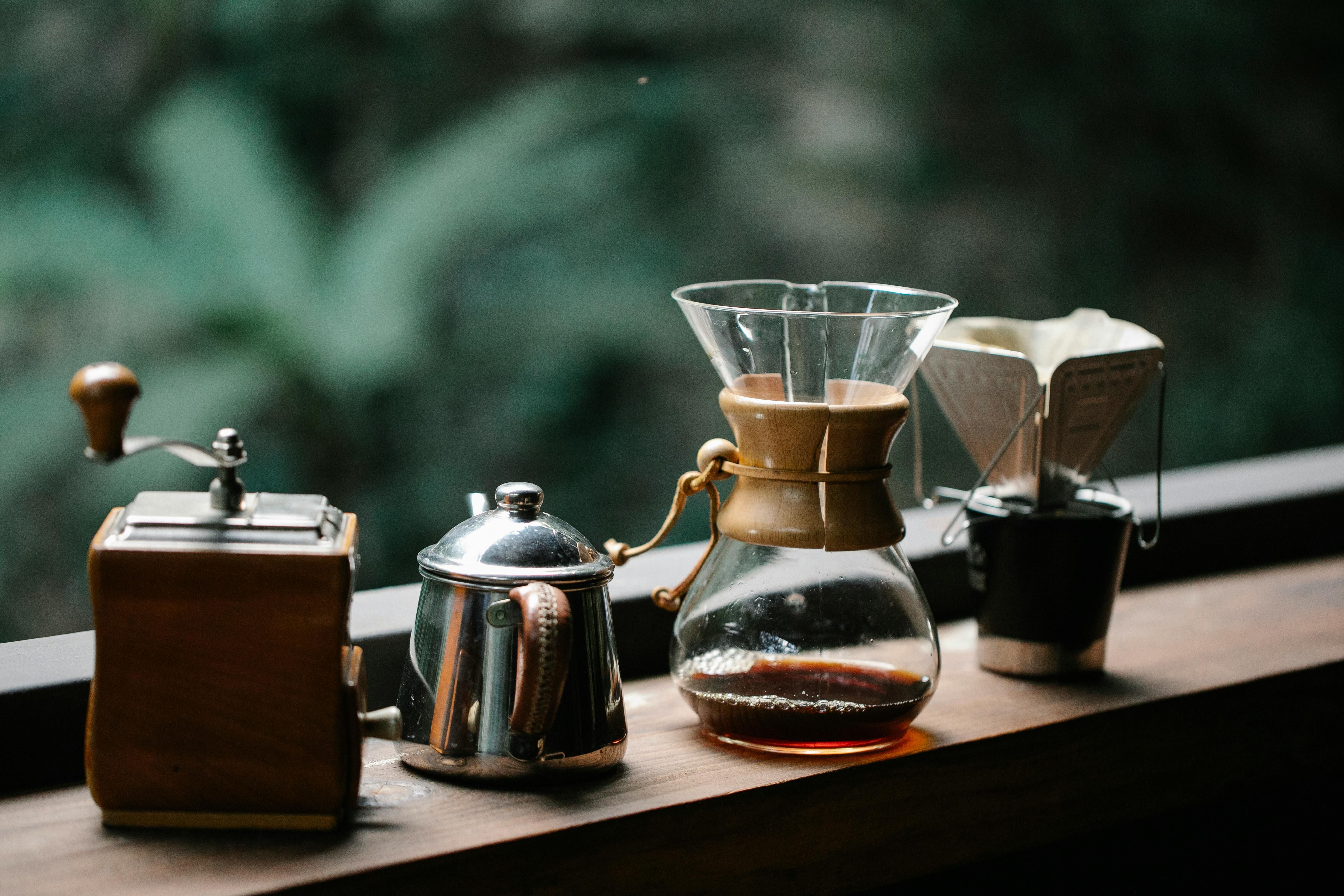 Cozy coffee setup featuring Chemex, kettle, and grinder on a wooden surface outdoors.